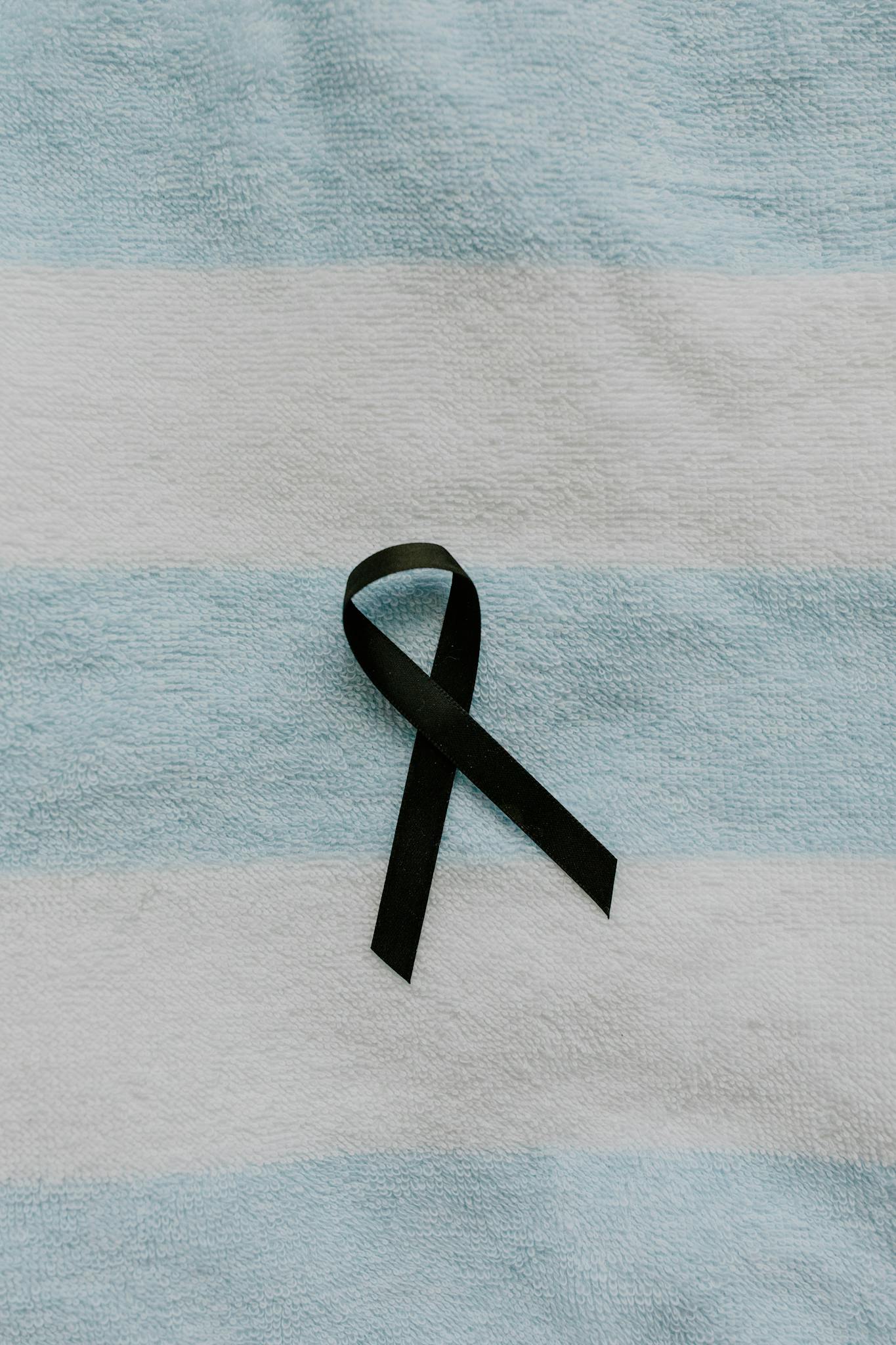 A black ribbon symbolizing mourning on a soft blue and white striped fabric background.