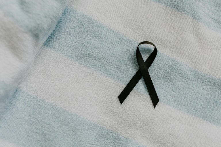 Black awareness ribbon placed on soft, striped fabric symbolizing support and remembrance.